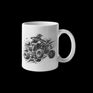 May include: White ceramic mug with a black and white illustration of a person riding an ATV. The ATV is in mid-air with the wheels off the ground. The person is wearing a helmet and goggles.
