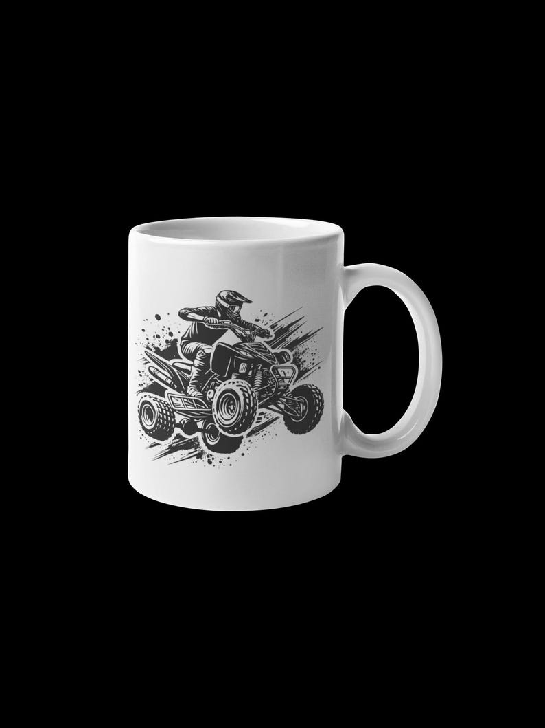 May include: White ceramic mug with a black and white illustration of a person riding an ATV. The ATV is in mid-air with the wheels off the ground. The person is wearing a helmet and goggles.