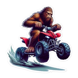 May include: A sticker featuring a brown Bigfoot riding a red ATV. The Bigfoot has a stern expression and is gripping the handlebars. The ATV has black tires and is kicking up a cloud of dust, suggesting speed and adventure.