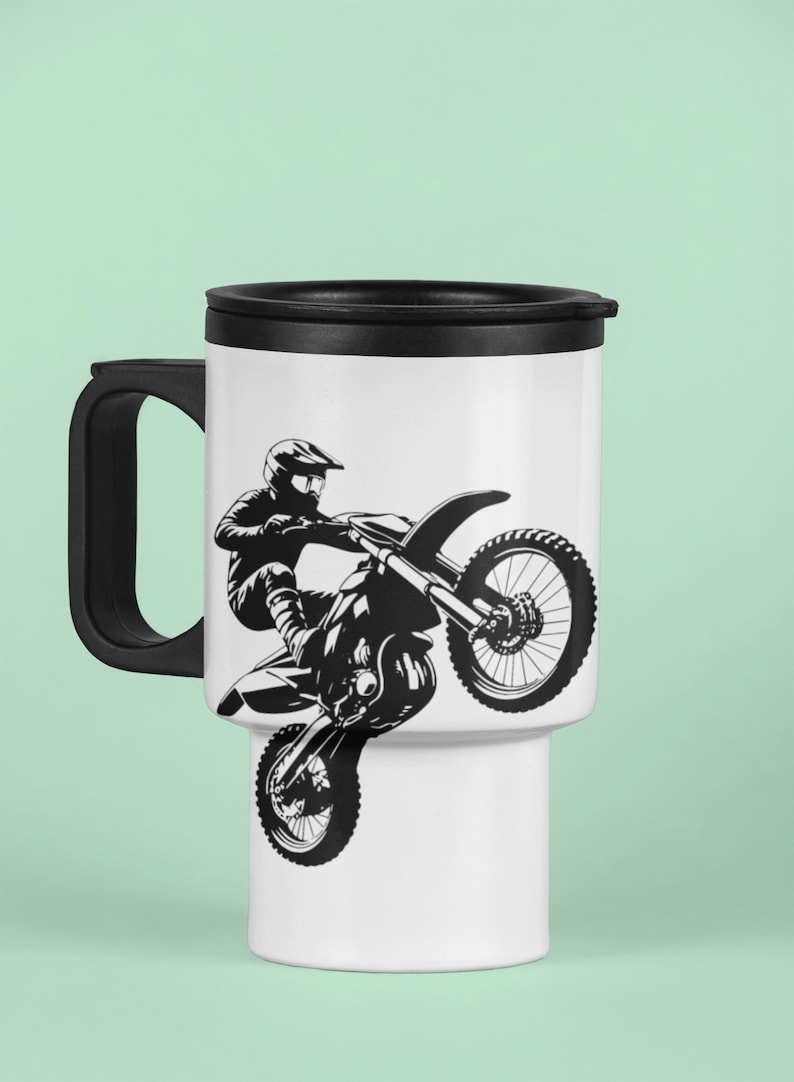 May include: A white travel mug with a black lid and handle. The mug features a black and white silhouette of a motocross rider performing a stunt.