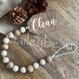 May include: A wooden bead garland with a brown wooden tag that says "Clean". The garland is made of brown and white beads and has a white string attached to it.