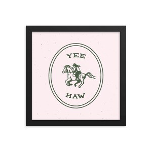 May include: A framed print with a pink background and a green illustration of a cowboy riding a horse inside a circle with the text "YEE HAW" in green.