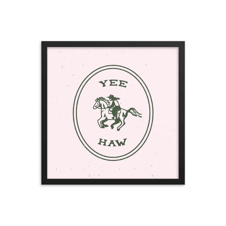 May include: A framed print with a pink background and a green circle containing a cowboy riding a horse. The circle has the words "YEE HAW" written inside.