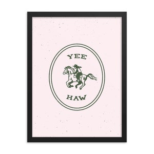 May include: A framed print with a pink background and a green circle containing a cowboy riding a horse. The circle has the words "YEE HAW" written inside.