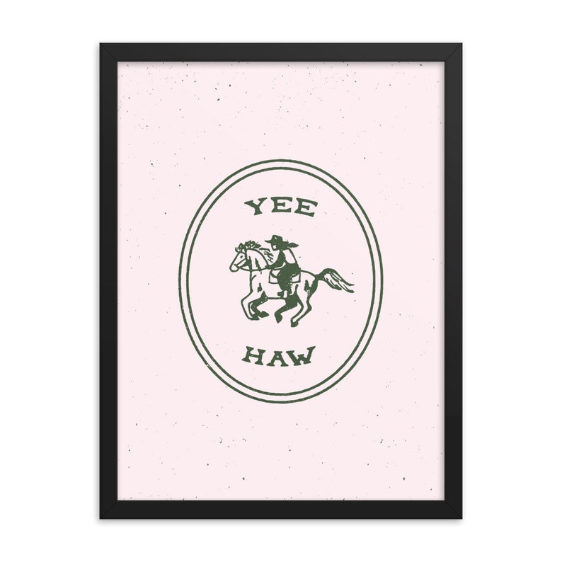 May include: A framed print with a pink background and a green circle containing a cowboy riding a horse. The circle has the words "YEE HAW" written inside.