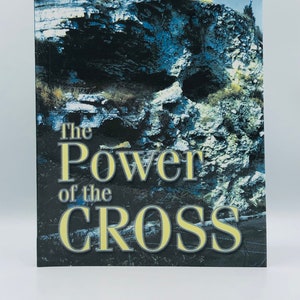 May include: Book cover with a blue and green rocky cliff with a cave opening. The title is "The Power of the Cross" in yellow text with the author "Dr. Robert Lindsted" in yellow text at the top.
