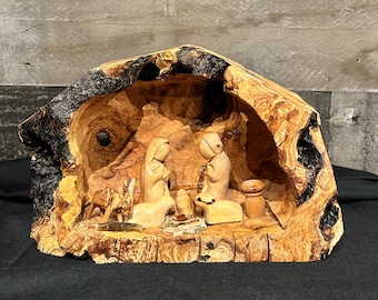Puede incluir: Un belén de madera tallado en una sola pieza de madera. La escena representa a María, José y el niño Jesús en un pesebre, con un buey y un burro. La madera tiene un color marrón claro natural con bordes de corteza oscura.