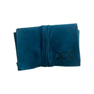 May include: Teal blue velvet pouch with a black triple moon symbol embroidered on the front. The pouch has a tie closure.