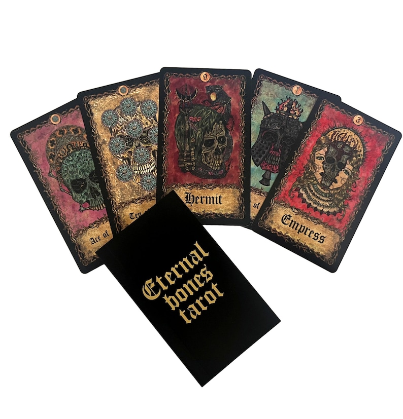 May include: A set of tarot cards with a black box that says "Eternal Bones Tarot". The cards feature dark, gothic imagery with skulls and skeletons. The cards are spread out on a white background.