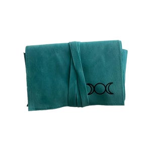 May include: Teal suede pouch with a black triple moon symbol. The pouch has a flap closure and a tie closure.