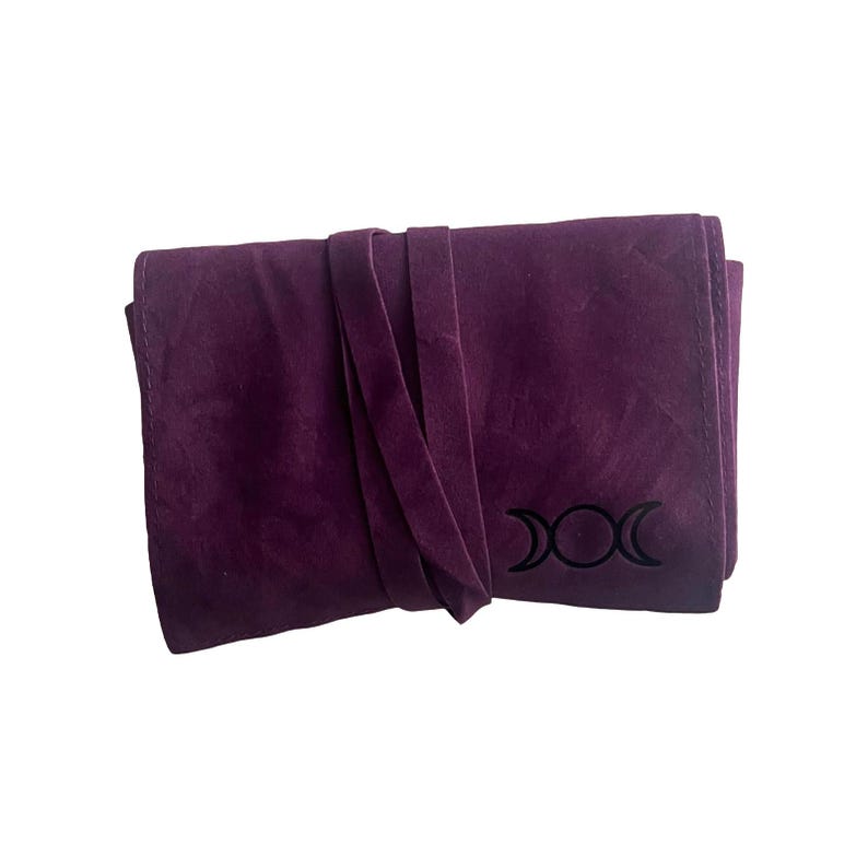 May include: A purple suede pouch with a black triple moon symbol. The pouch has a flap closure and a tie closure.