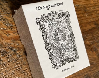 May include: A white box with black text and illustrations. The box contains a tarot deck called "The Magic Gate Tarot" and includes 78 cards and a guide.