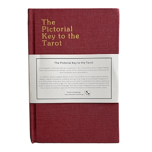 Puede incluir: La Llave Pictórica del Tarot, un libro de tapa dura color burdeos con letras doradas en la portada y el lomo. La contraportada presenta una etiqueta blanca con texto que describe la historia y los detalles de publicación del libro.