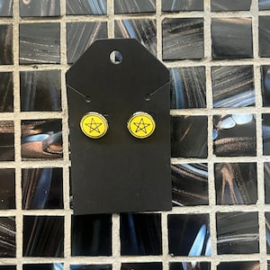 May include: A pair of yellow and black pentagram stud earrings on a black card.