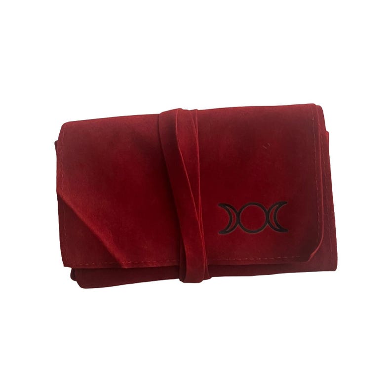May include: A red velvet pouch with a black triple moon symbol. The pouch has a tie closure.