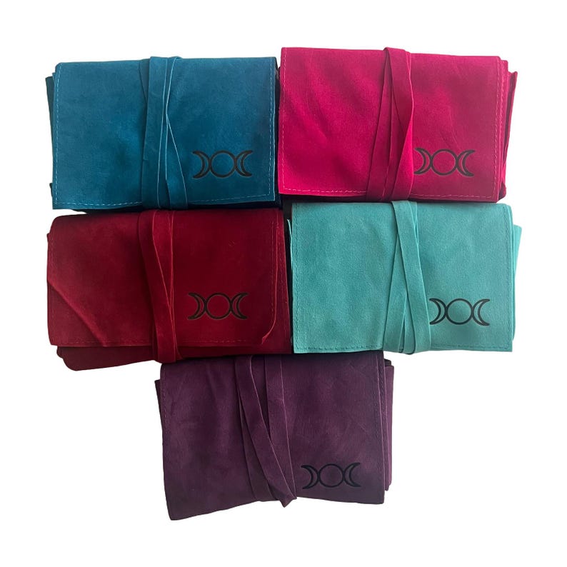 May include: Five different colored velvet pouches with a triple moon symbol embroidered on each. The pouches are folded and stacked on top of each other. The colors are teal, pink, red, light blue, and purple.