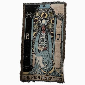 May include: A tapestry featuring the High Priestess card from the tarot deck. The card depicts a woman wearing a blue robe and a crown with a crescent moon. She is seated between two pillars, one black and one white, with the letters B and J on them. The card is framed with a brown border and has a fringe.
