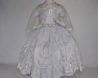 May include: White satin dress with a lace overlay and a silver beaded belt. The dress has a cape and a design of the Virgin Mary on the front.