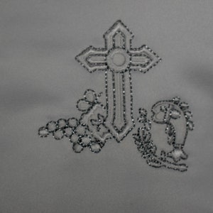 May include: A white fabric with a silver embroidered cross, grapes, and a fish design.