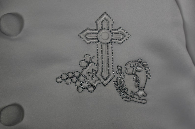May include: A white fabric with a silver embroidered cross, grapes, and a fish design.