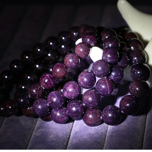 Op de afbeelding: Close-up van meerdere armbanden met kralen. De armbanden hebben donkerpaarse en zwarte kralen met een glanzende afwerking. De kralen zijn rond en lijken van gepolijste steen te zijn. De armbanden zijn in lagen gerangschikt, wat een visueel aantrekkelijke weergave creëert.