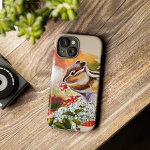 May include: A phone case with a watercolor painting of a chipmunk eating red berries. The chipmunk is brown and white with a bushy tail. The background is a soft orange and yellow with white flowers.