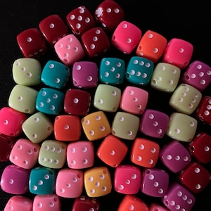May include: A collection of colorful dice with white dots. The dice are made of plastic and are in various shades of red, pink, green, orange, and yellow.