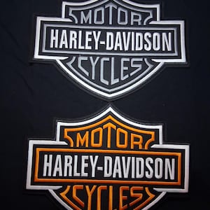 May include: Two Harley-Davidson patches. The top patch is white, gray, and black. The bottom patch is orange, white, and black. Both patches have the words "MOTOR", "HARLEY-DAVIDSON", and "CYCLES".