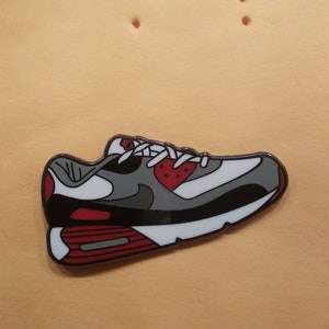 Könnte beinhalten: Ein Emaille-Pin mit einem Nike Air Max 90 Schuh in Rot, Weiß und Grau.