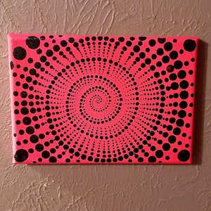 May include: A pink canvas painting with a black and white dot pattern. The dots are arranged in a spiral pattern, creating a sense of movement and depth.