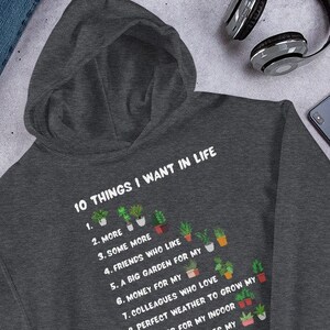 May include: A dark grey hooded sweatshirt with a white graphic print that reads "10 THINGS I WANT IN LIFE" and lists 10 items with plant emojis.