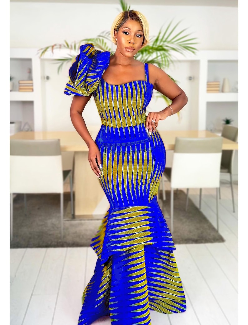 May include: A floor-length mermaid dress in a vibrant royal blue and olive green geometric print. The dress features a square neckline, one thick shoulder strap, and a large, ruffled architectural accent on the opposite shoulder.