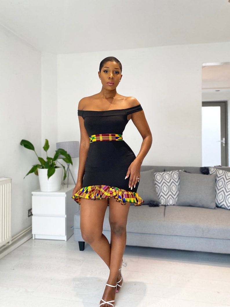 Puede incluir: Un vestido negro de hombros descubiertos con un dobladillo con volantes. El vestido tiene una cintura estampada de colores y un dobladillo con volantes.