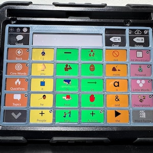 May include: A black tablet with a blue and white grid interface. The interface features colorful buttons with words and icons for communication. The tablet is designed for augmentative and alternative communication.
