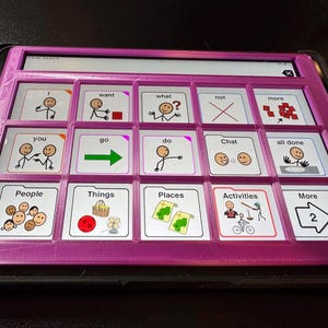 May include: A pink tablet case with a grid of communication symbols. The symbols include words like "want," "go," and "people," each paired with a corresponding image. The tablet is designed for communication and educational purposes.