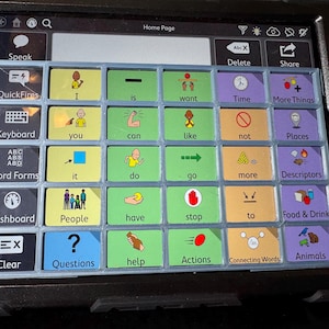 May include: A black tablet with a grid of colorful buttons for communication. Buttons include words like "Speak," "Keyboard," and "Questions," along with icons. The screen displays "Home Page" at the top.