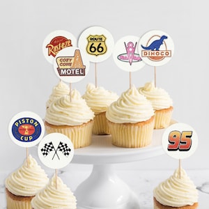 May include: A set of six cupcakes decorated with various Cars themed toppers, including the Cozy Cone Motel, Route 66, Dinoco, Piston Cup, and the number 95. The cupcakes are topped with white frosting and are arranged on a white cake stand.