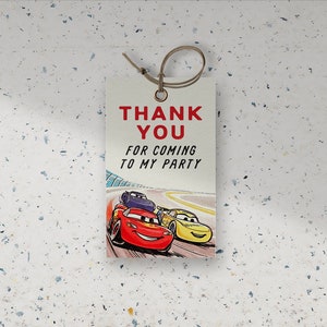 Può includere: Un'etichetta di ringraziamento bianca con testo rosso che dice "Grazie per essere venuto alla mia festa". L'etichetta presenta un'immagine di cartone animato di Saetta McQueen e Cricchetto del film Cars che corrono su una pista.