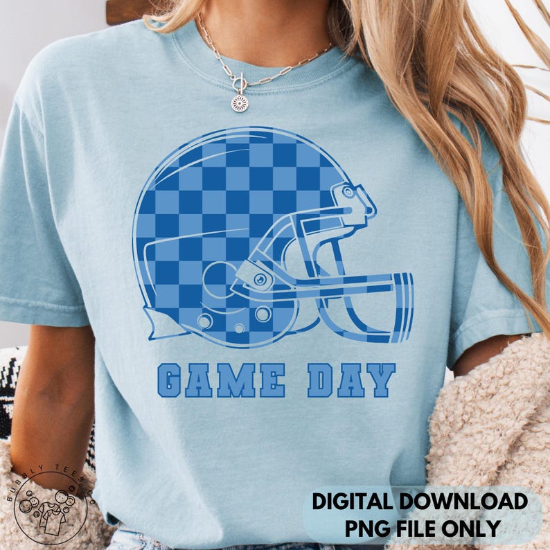 May include: Light blue t-shirt featuring a blue football helmet graphic with a checkered pattern. The words "GAME DAY" are printed in blue below the helmet. The shirt is a digital download, PNG file only.