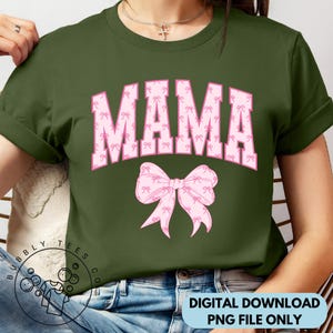 Puede incluir: Una camiseta verde con la palabra "MAMA" en letras rosas con un patr&oacute;n de lazo rosa. Las letras est&aacute;n delineadas en blanco y tienen una fuente de estilo universitario.