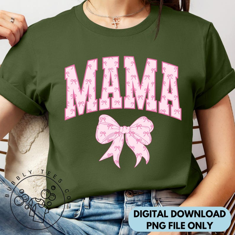 Puede incluir: Una camiseta verde con la palabra "MAMA" en letras rosas con un patr&oacute;n de lazo rosa. Las letras est&aacute;n delineadas en blanco y tienen una fuente de estilo universitario.