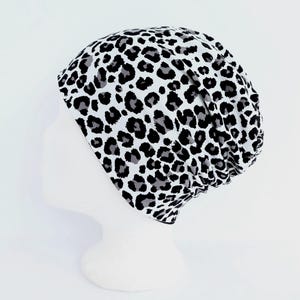 Könnte beinhalten: Ein weißer Beanie mit einem schwarzen und grauen Leopardenmuster. Der Beanie wird auf einem weißen Schaufensterkopf präsentiert. Der Stoff hat ein weiches, leicht strukturiertes Aussehen.
