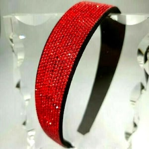 May include: A red headband with a sparkly finish. The headband is made of a black elastic band with a red rhinestone trim.