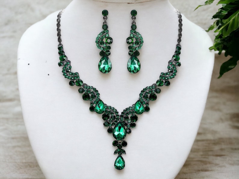May include: A green crystal necklace and earrings set with a teardrop pendant. The necklace features a delicate, intricate design with a silver chain.