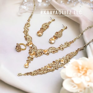 May include: A gold-toned jewelry set featuring a necklace, bracelet, earrings, and ring. The set is adorned with amber-colored gemstones and intricate detailing. The text "#KAAYAGLITZ LLC" is visible in the image.