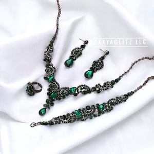 May include: A green emerald jewelry set with a necklace, bracelet, earrings, and ring. The jewelry is made of dark metal and features a floral design with teardrop-shaped stones.