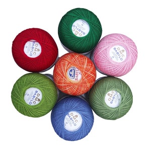 Può includere: Sette gomitoli di filo DMC Babylo in vari colori: verde, rosso, rosa, arancione, blu e due tonalità di verde. Ogni gomitolo ha un'etichetta bianca con il logo DMC e il testo "BABYLO" e "20g".