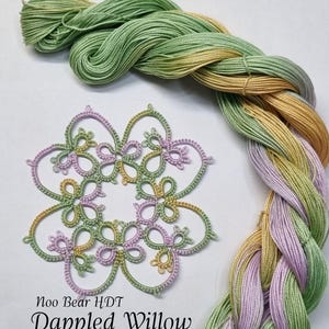 以下が含まれることがあります： 緑、黄色、紫のグラデーションの糸の玉。糸の名前は「Dappled Willow」で、「Moo Bear HdT」の製品です。