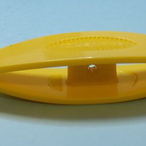 Op de afbeelding: Een gele plastic haaknaald draadtrekker. De draadtrekker heeft de vorm van een vis met een klein gaatje in het midden.