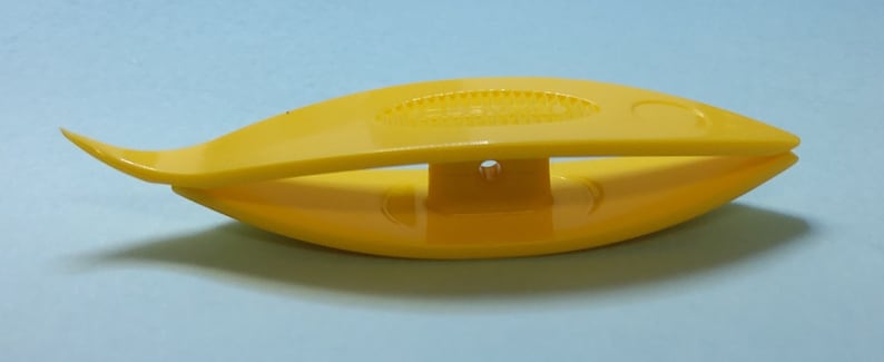 Op de afbeelding: Een gele plastic haaknaald draadtrekker. De draadtrekker heeft de vorm van een vis met een klein gaatje in het midden.